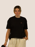 Frau in schwarzem Heavy Tee „How To Stay Awake Forever“ von Bengel & Göre, Vorderseite mit Brust-Stick, hält Coffee-to-go.