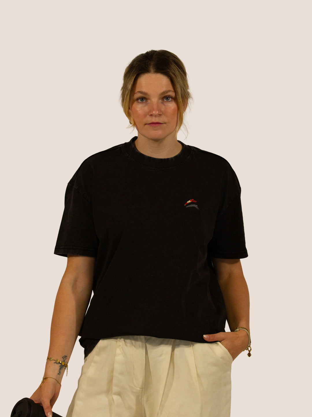 Frau in schwarzem Heavy Tee „How To Stay Awake Forever“ von Bengel & Göre, Vorderseite mit Brust-Stick, hält Coffee-to-go.