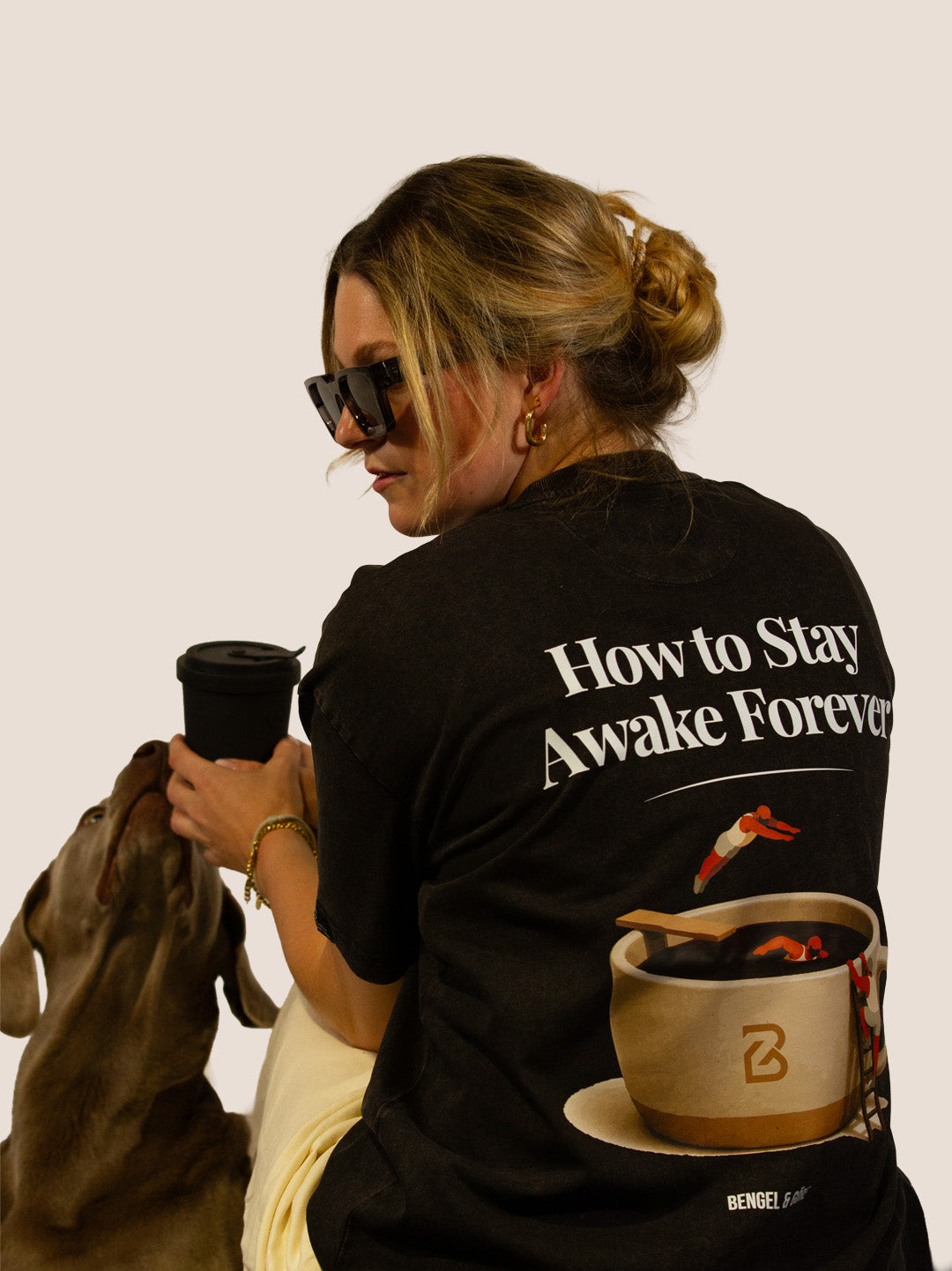 Frau im schwarzen „How To Stay Awake Forever“ Heavy Tee mit Weimaraner-Hund, Kaffeetassen-Rückenprint.