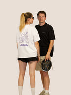 Paar in Bengel & Göre Rennrad-Heavy-Tees: Frau in Off-White mit lila Print hinten, Mann in Schwarz vorn.