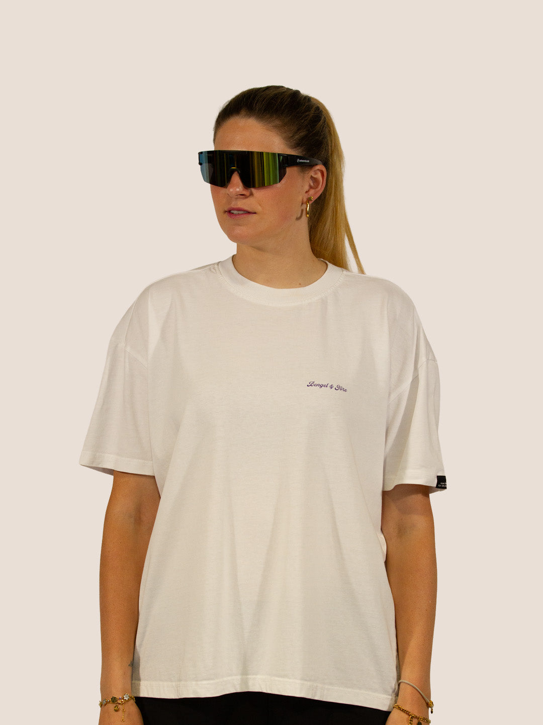 Frau im Off-White Bengel & Göre Heavy Tee mit Sport-Sonnenbrille, Brust-Schriftzug vorn.