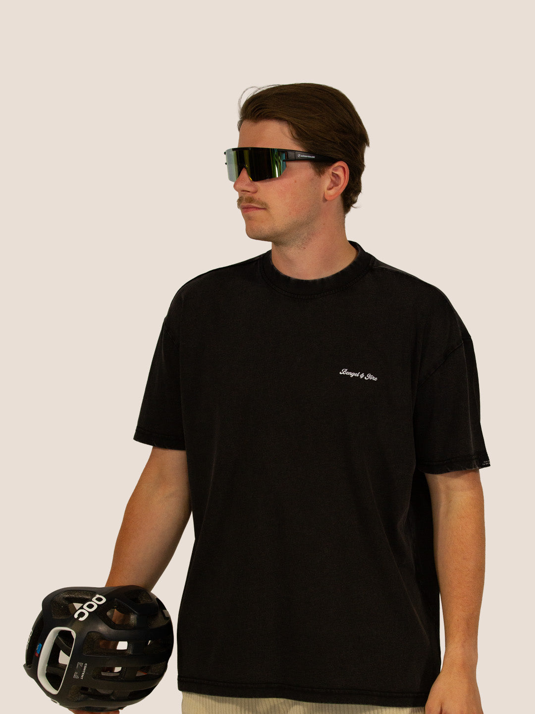 Mann im schwarzen Bengel & Göre Heavy Tee mit Brust-Schriftzug, Rennrad-Brille und POC-Helm, Vorderseite.