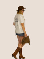 Frau im Off-White „How To Lose Money On Horses“ Heavy Tee mit Filzhut und Cowboystiefeln, Seitenansicht.