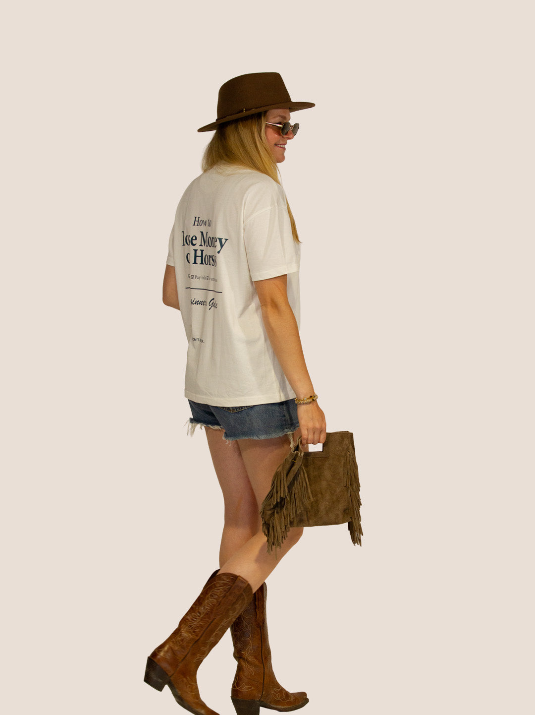 Frau im Off-White „How To Lose Money On Horses“ Heavy Tee mit Filzhut und Cowboystiefeln, Seitenansicht.