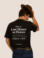 Mann im schwarzen „How To Lose Money On Horses“ Heavy Tee von Bengel & Göre, Rückenprint, lüftet den Filzhut.