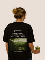 Rückseite des schwarzen Heavy Tee „Kyoto Morning Matcha Club“ mit grünem Kyoto-Foto-Print, Frau mit Matcha.