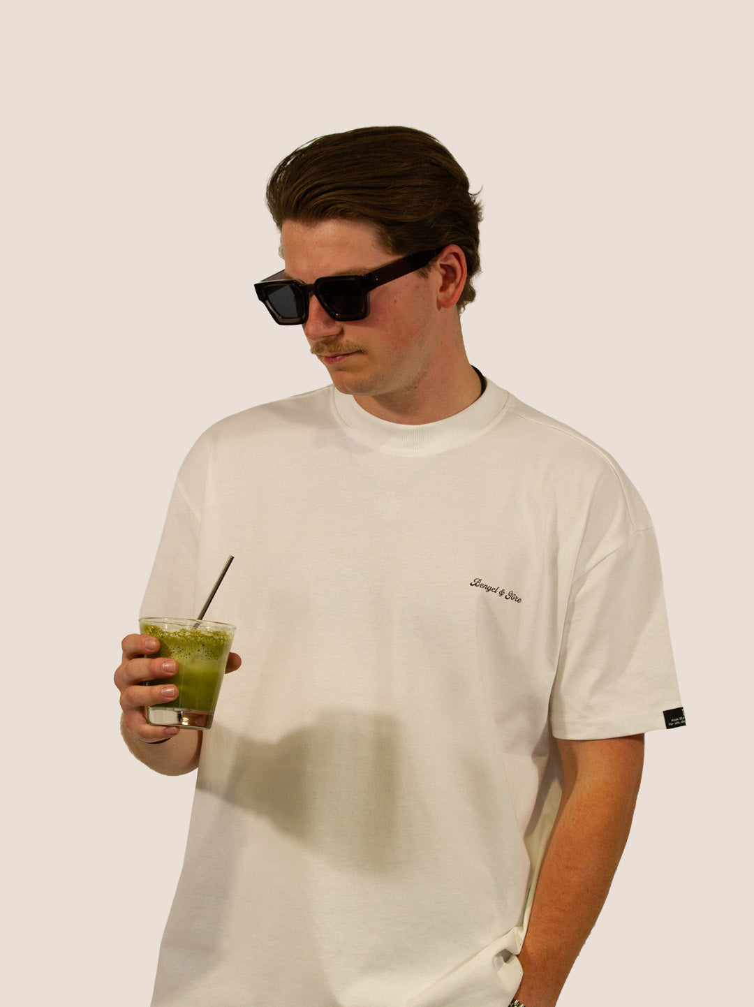 Mann im Off-White Heavy Tee von Bengel & Göre mit Matcha-Drink und Sonnenbrille, Kyoto Morning Matcha Club.