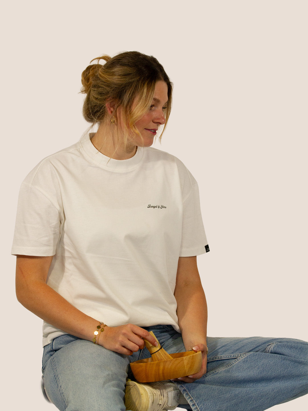 Frau im Off-White Bengel & Göre Heavy Tee mit Matcha-Schale und Bambusbesen, Vorderseite.