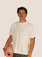 Mann im Off-White Bengel & Göre Heavy Tee mit Brust-Schriftzug und rosa Pilatesmatte, Vorderseite.