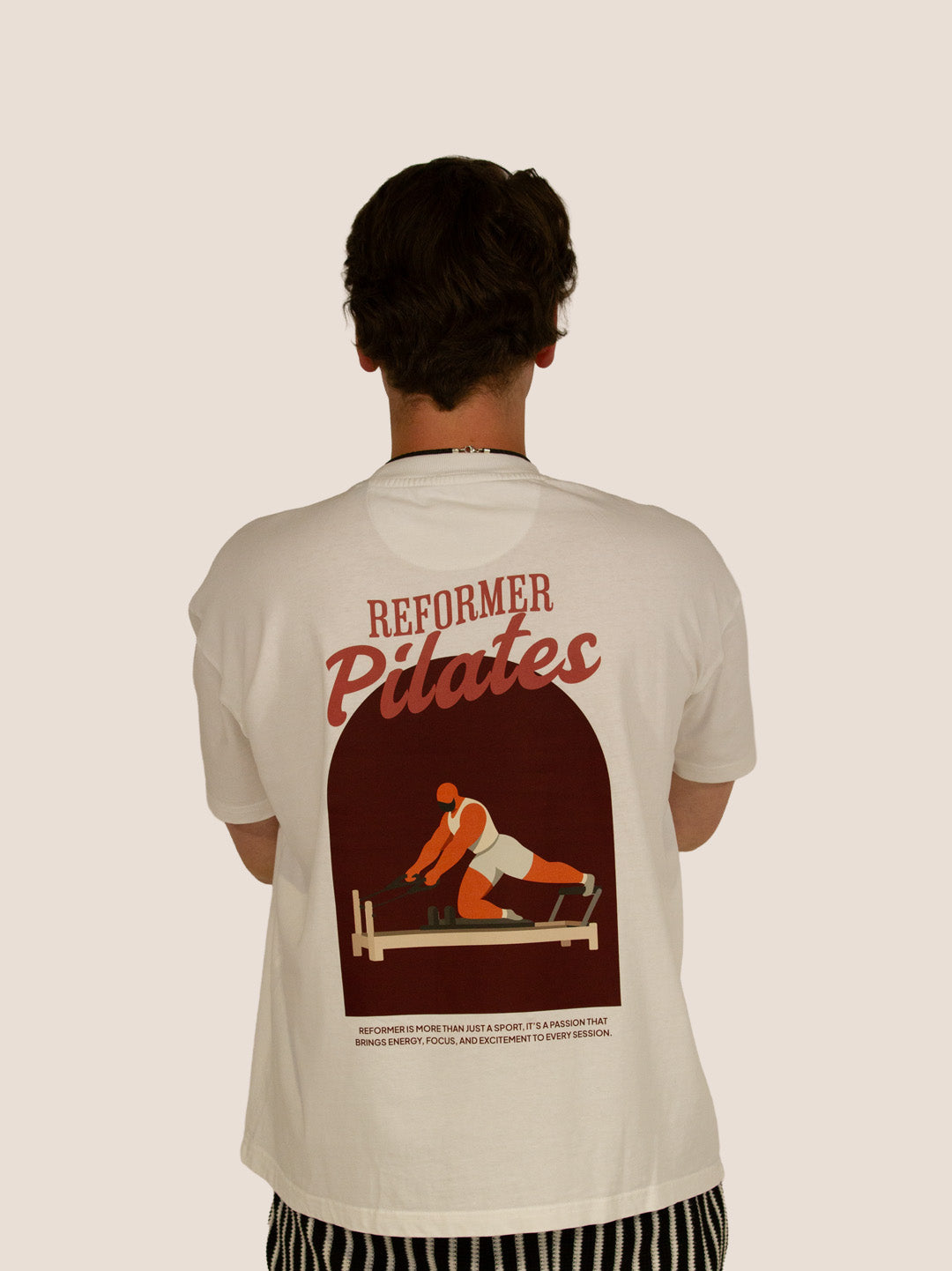 Rückseite des Off-White Heavy Tee „Reformer Pilates“ mit Reformer-Print im Bogen, Mann.