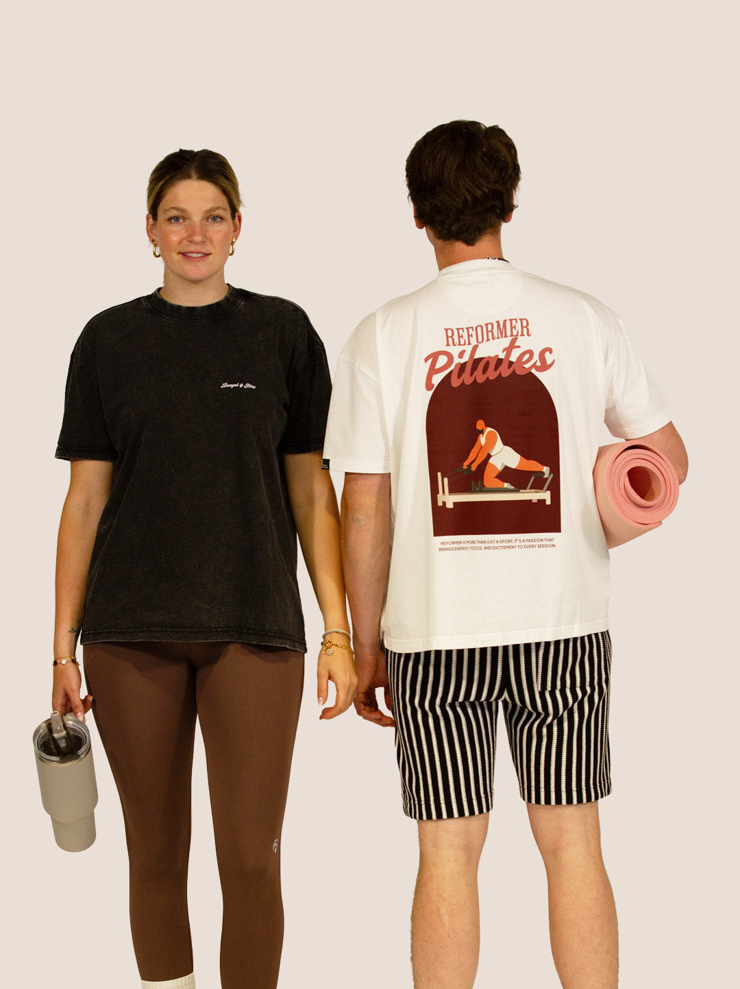 Paar in Bengel & Göre „Reformer Pilates“ Heavy Tees in Schwarz und Off-White mit rosa Pilatesmatte.