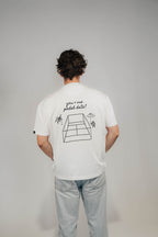 Rückansicht Mann im Off-White Heavy Tee „You + Me Padel Date“ mit Padel-Court-Zeichnung.